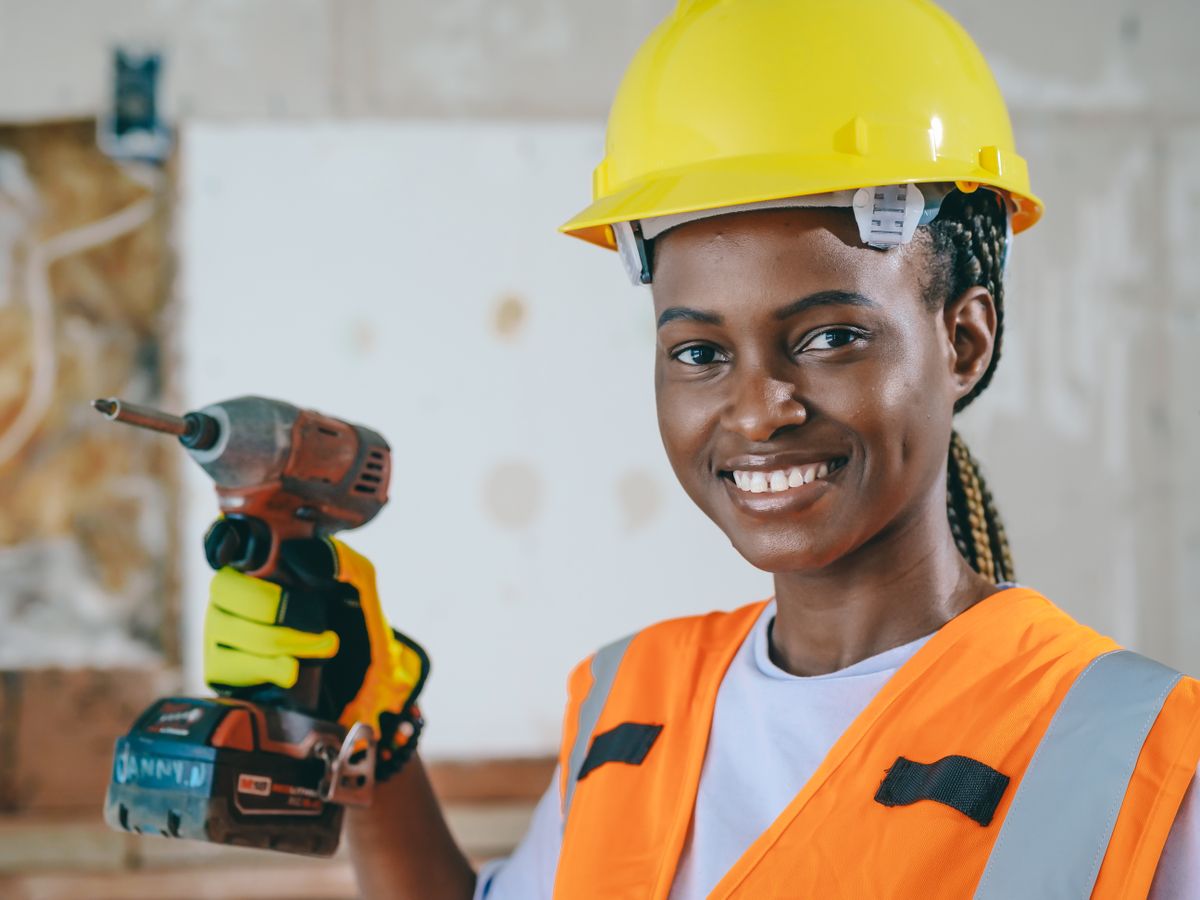 Smiling tradeswoman in a hard hat holding a power drill